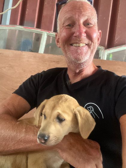 Man in black t-shirt holding a tan puppy indoors near a wooden wall